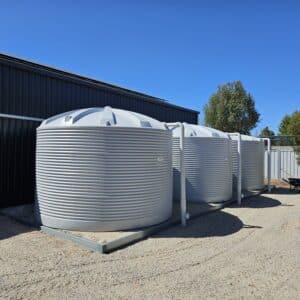 Three light grey Polymaster water tanks installed beside a shed, pipework visible